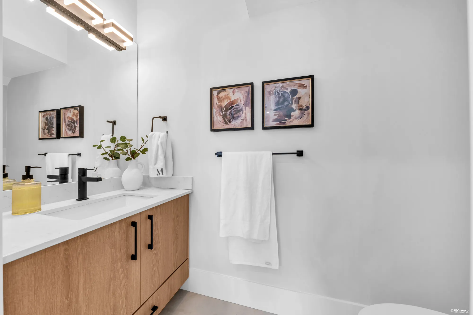The main-floor half bathroom: an oak vanity under a wide mirror, a towel bar, two framed prints