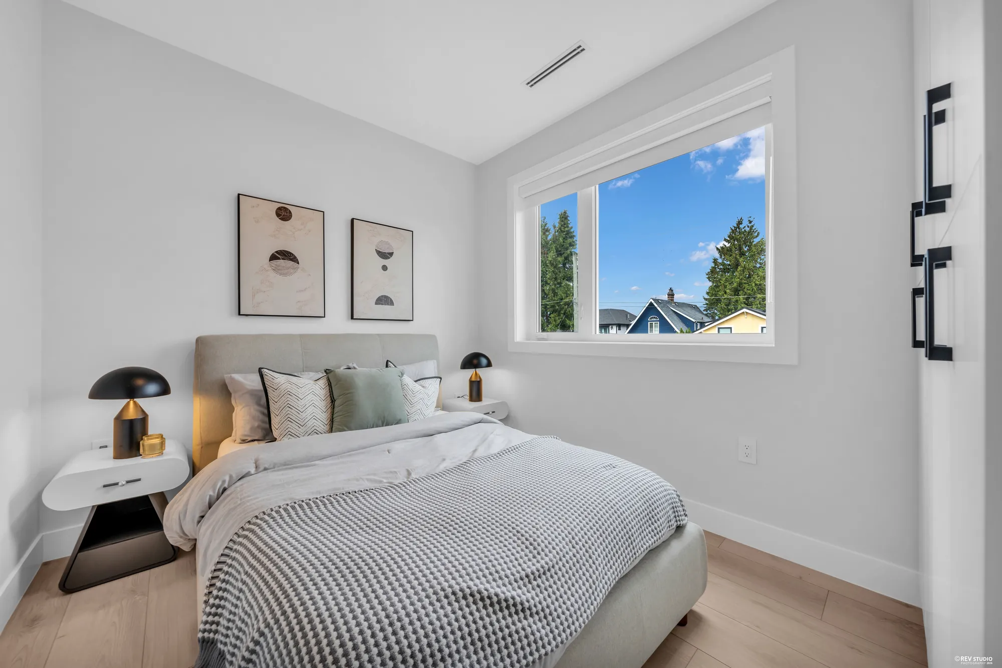 A bedroom with a double bed under two framed prints, the window in the far wall, a lamp on the night table