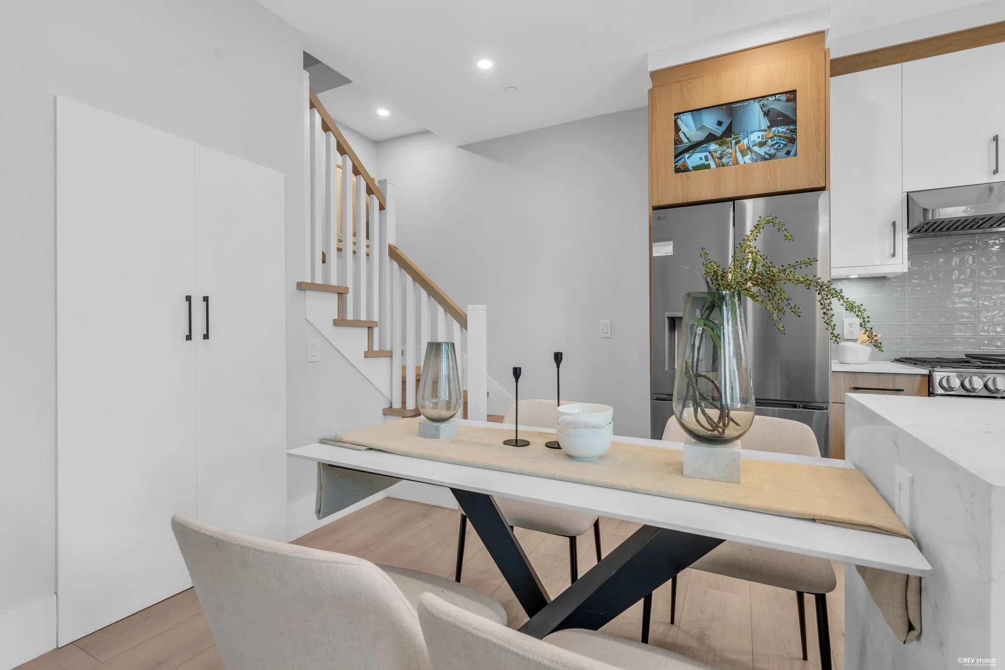 From the foyer: the dining table by the stair, the kitchen and its window beyond, a television on the wall