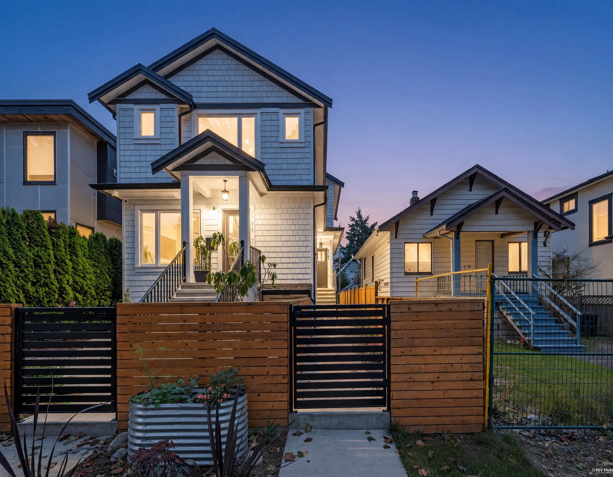2743 McGill Street at dusk: a new three-level house in white shingle and board with black trim, every window lit, behind a cedar fence with a black gate