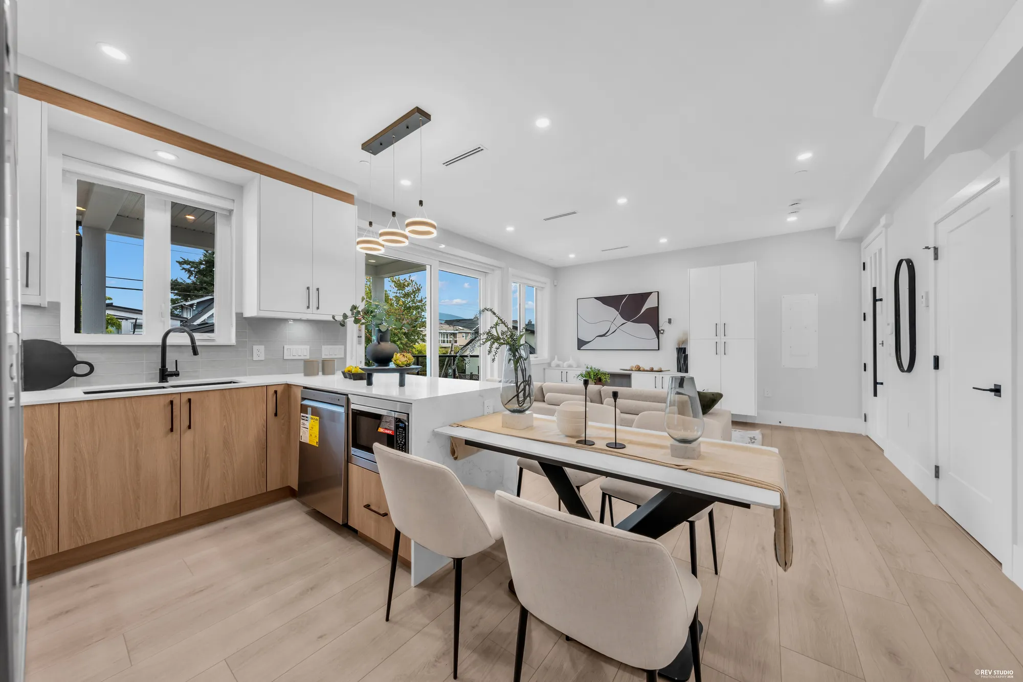 The kitchen and dining area: white upper cabinets, oak-look lower cabinets, white quartz counters, a gas range under the hood, the peninsula with its seats, gold ring pendants