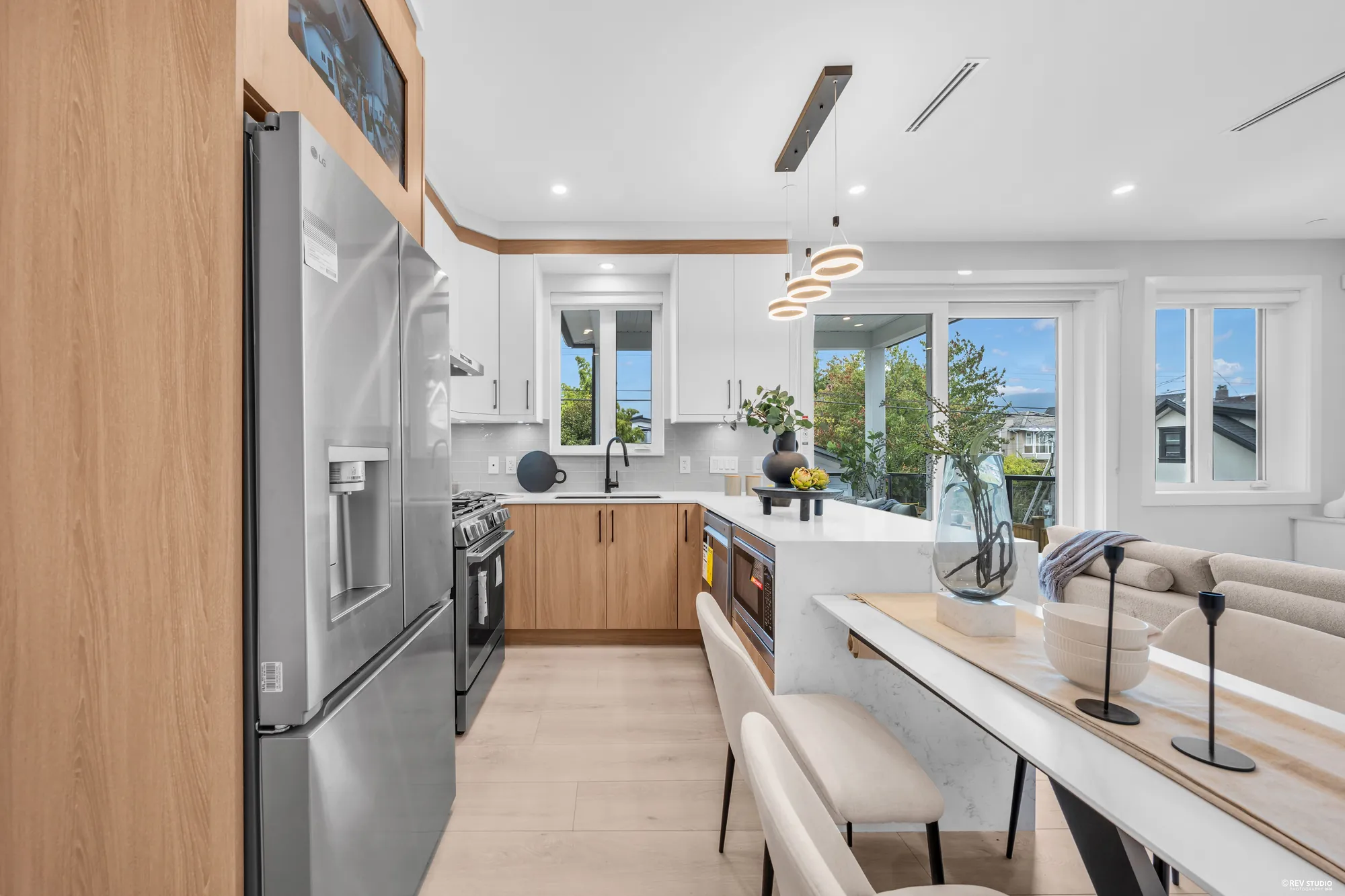 The kitchen from the fridge end: the stainless fridge, the counters, the window over the sink, the balcony doors beyond