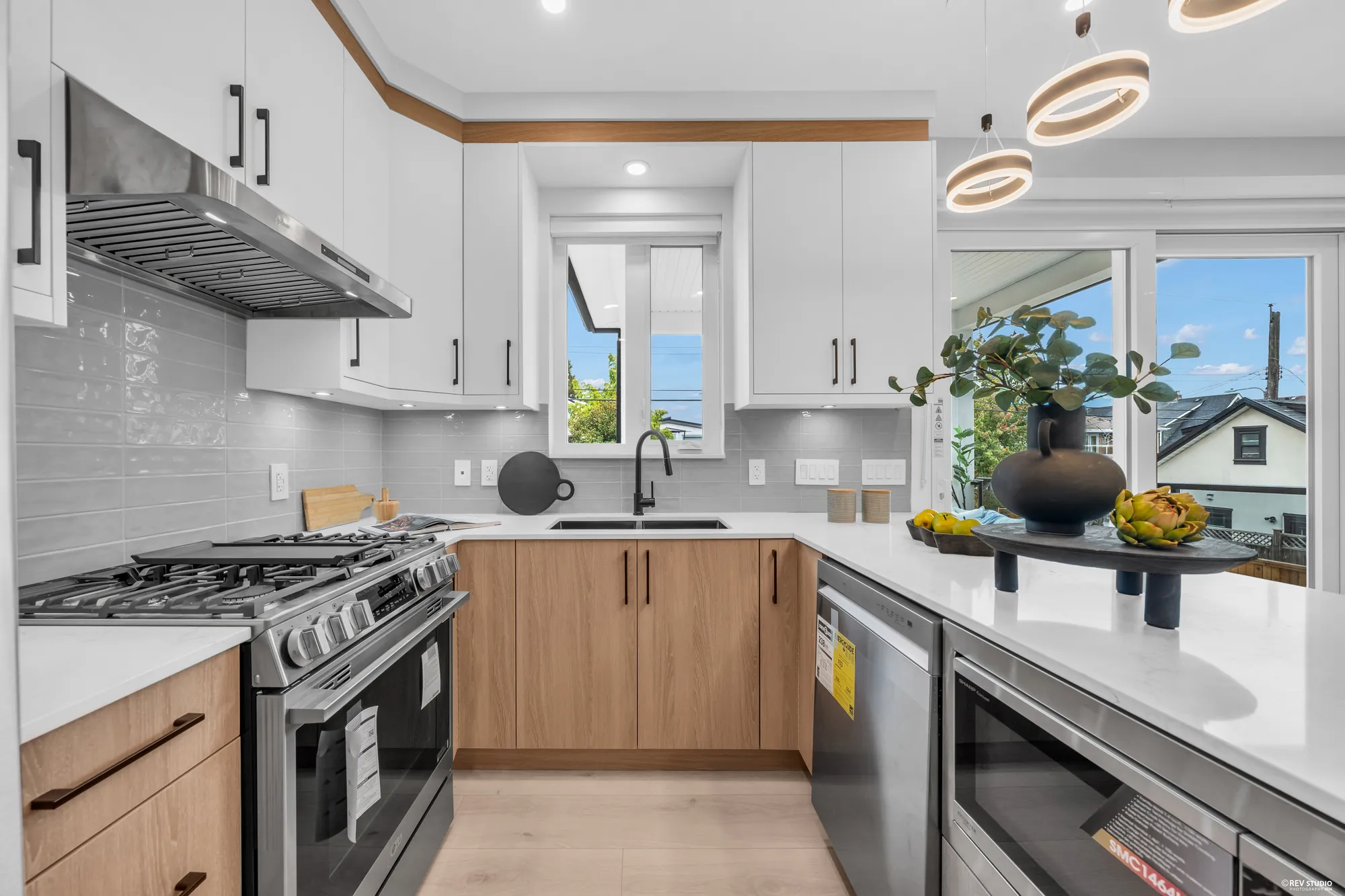 The range wall: a stainless gas range under the hood, a tiled backsplash, the sink under its window
