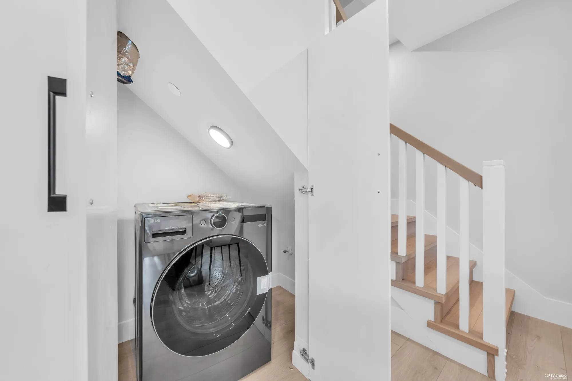 The laundry closet under the stair with a front-loading machine, the stair rail beside it