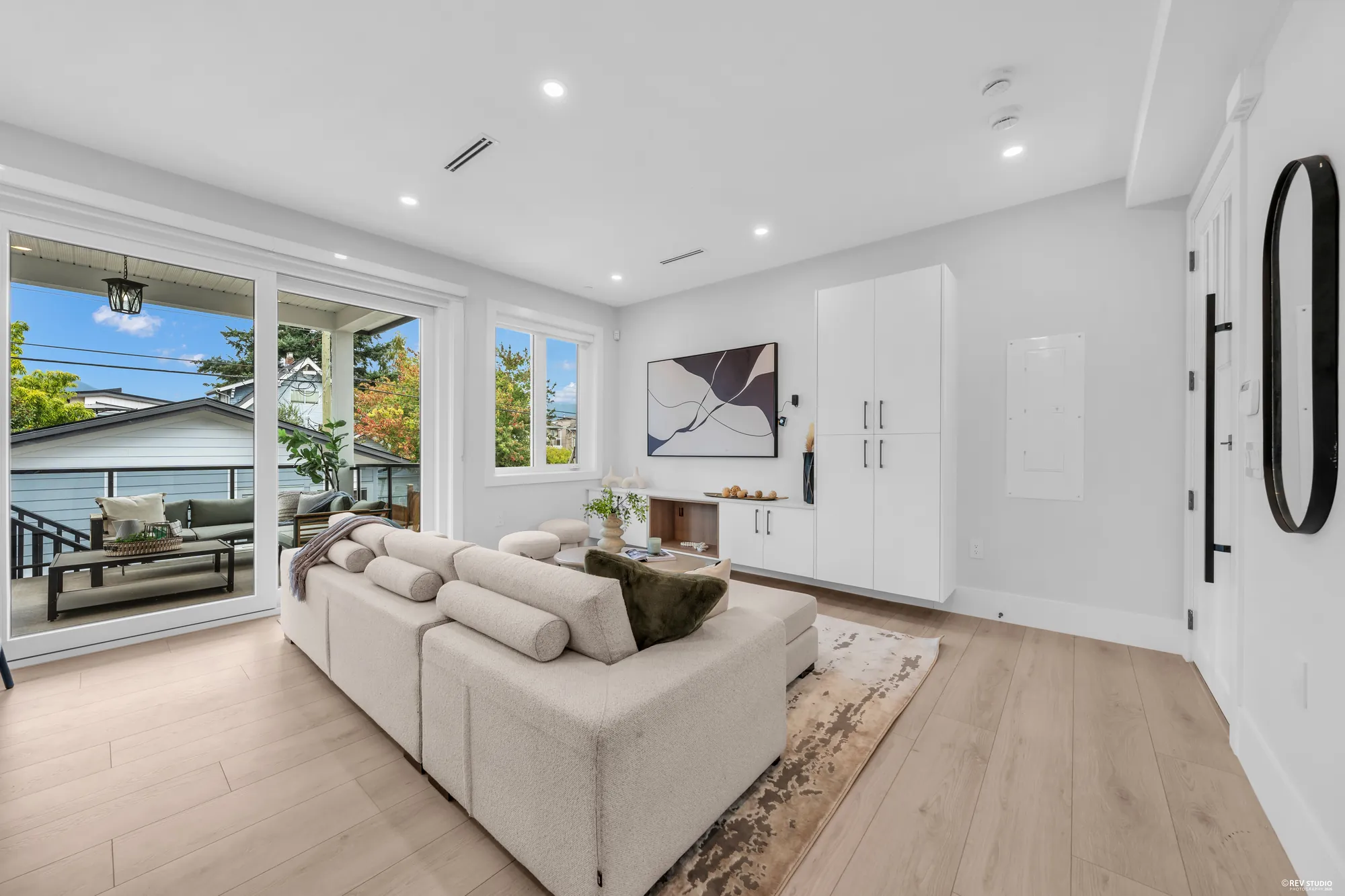 The living room: a pale sectional on a rug, a wall of white built-in cabinets with a long shelf, glass doors open to the covered balcony