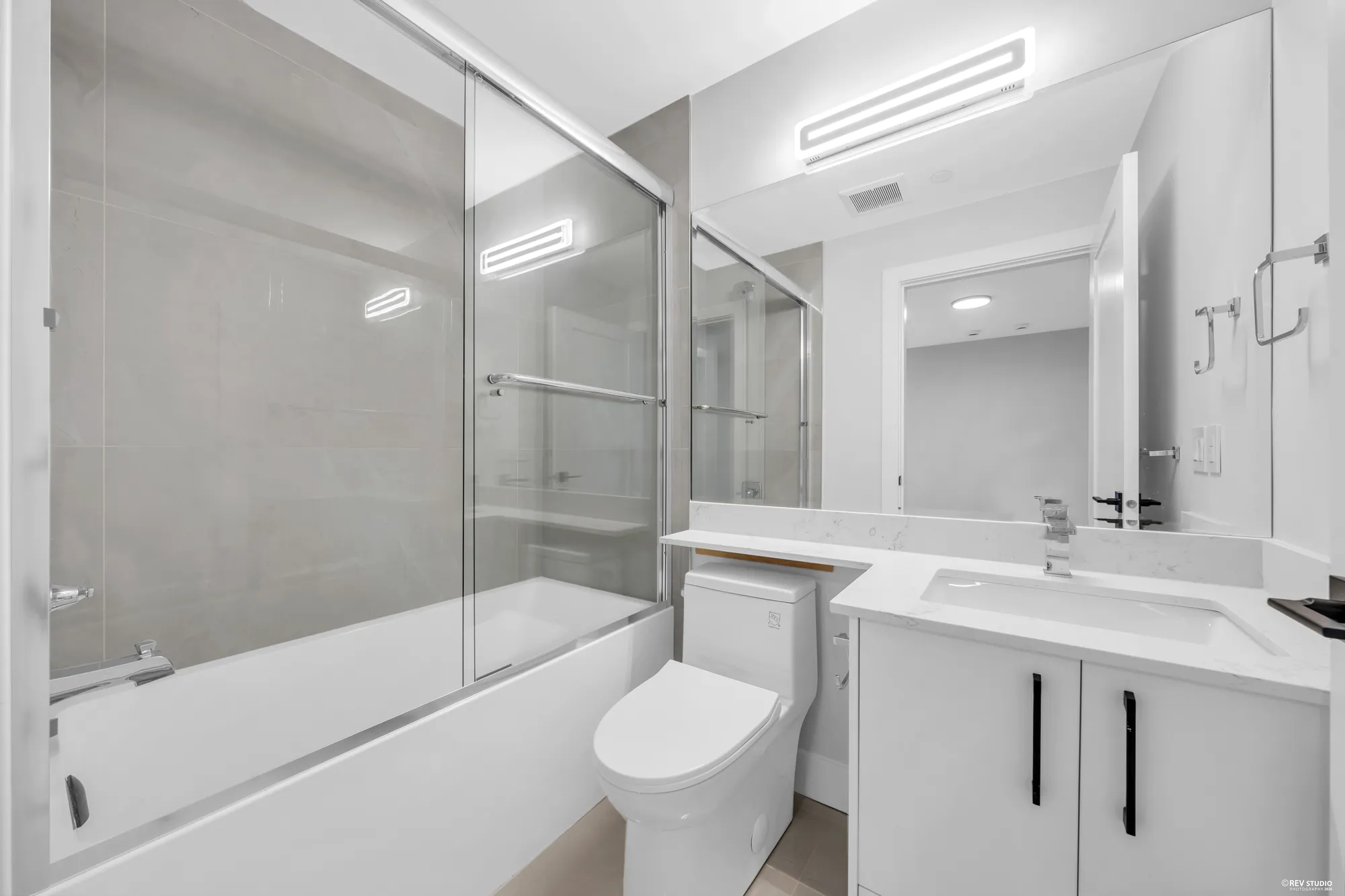 The lower bathroom: a tub behind a glass screen, a white vanity, a mirror with a light bar