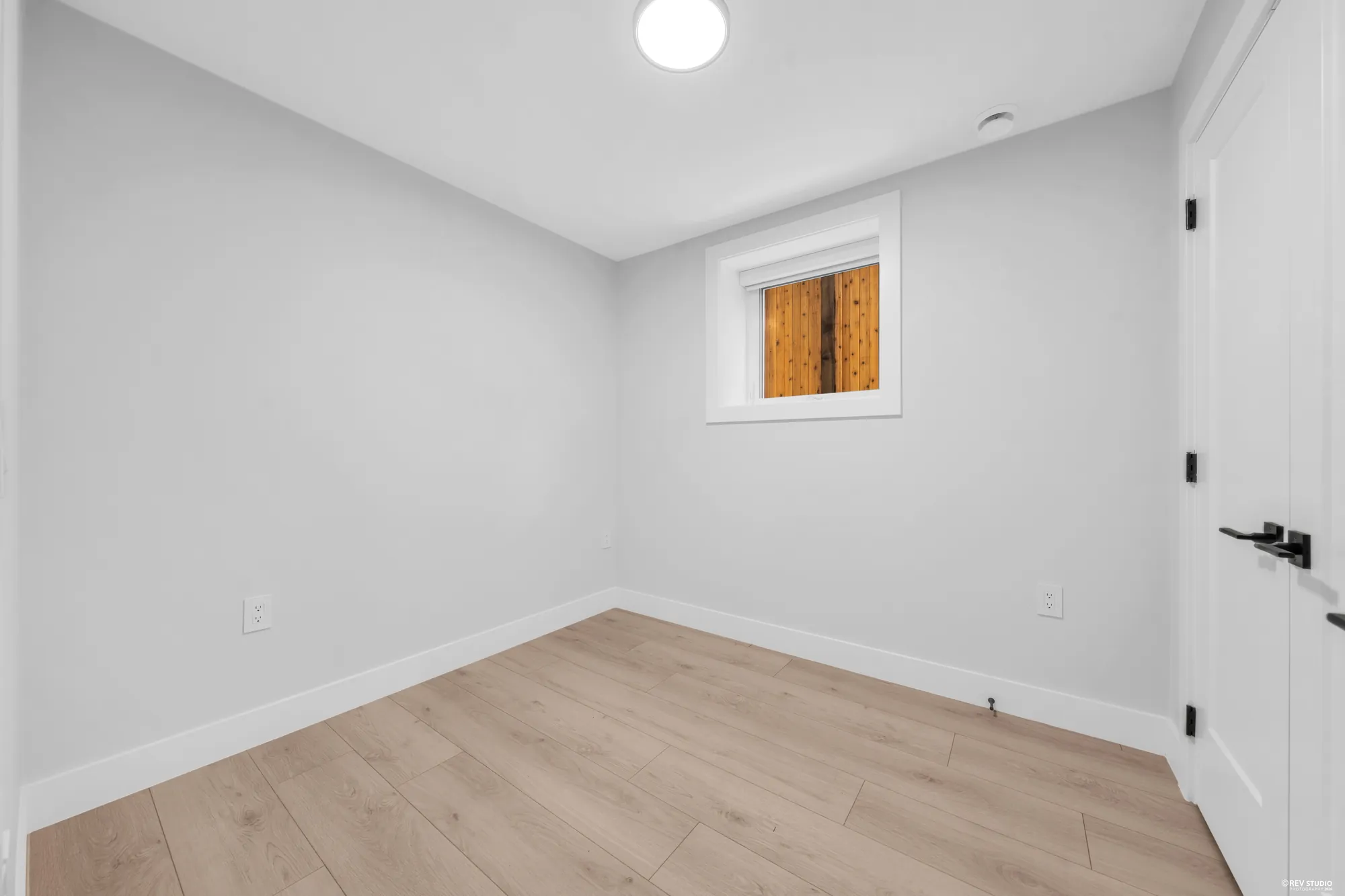 The lower bedroom: an empty room with laminate floor, a small window and a black-trimmed door