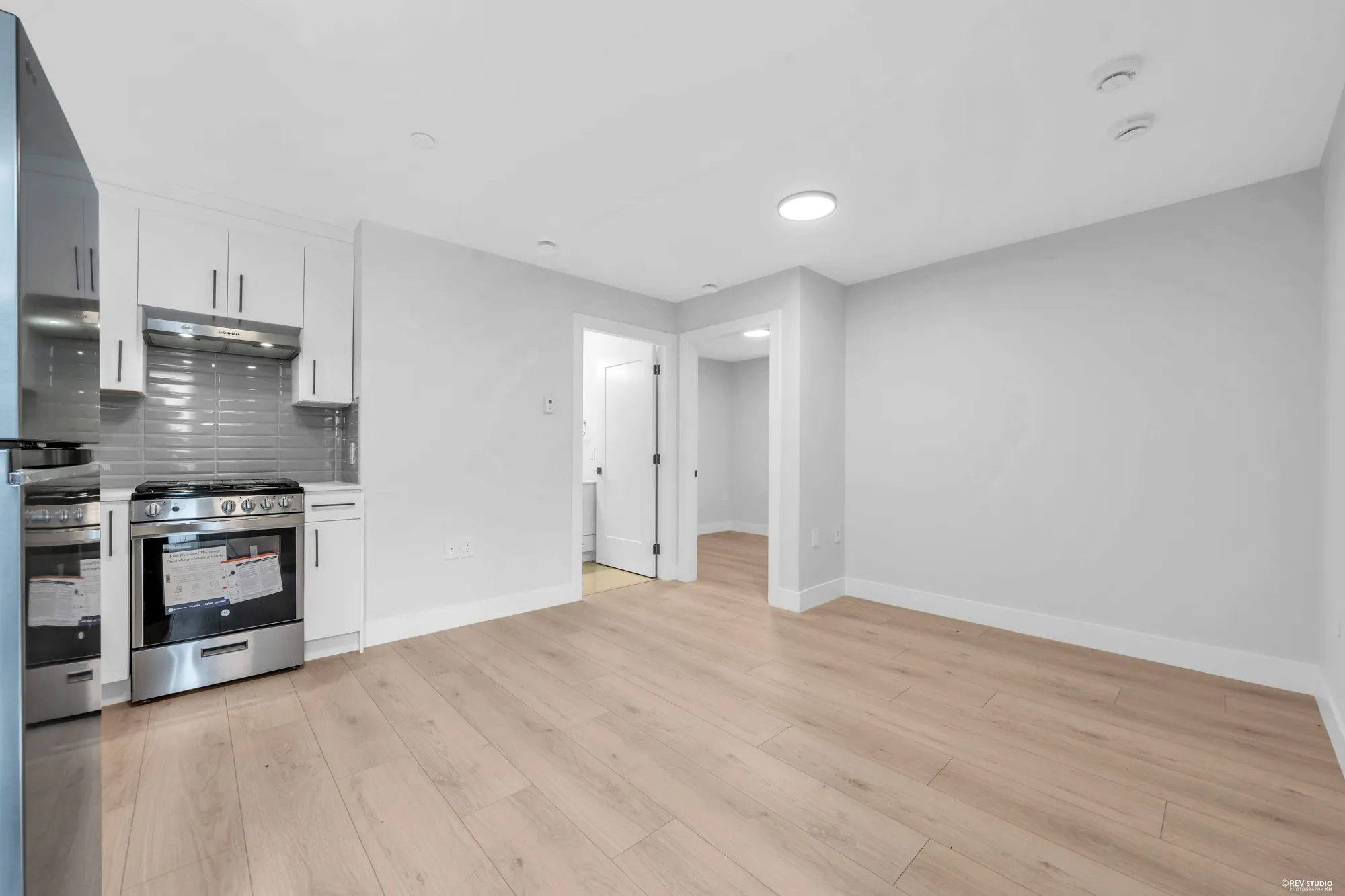 The lower kitchen: white cabinets, a stainless range and fridge along one wall, a window over the counter