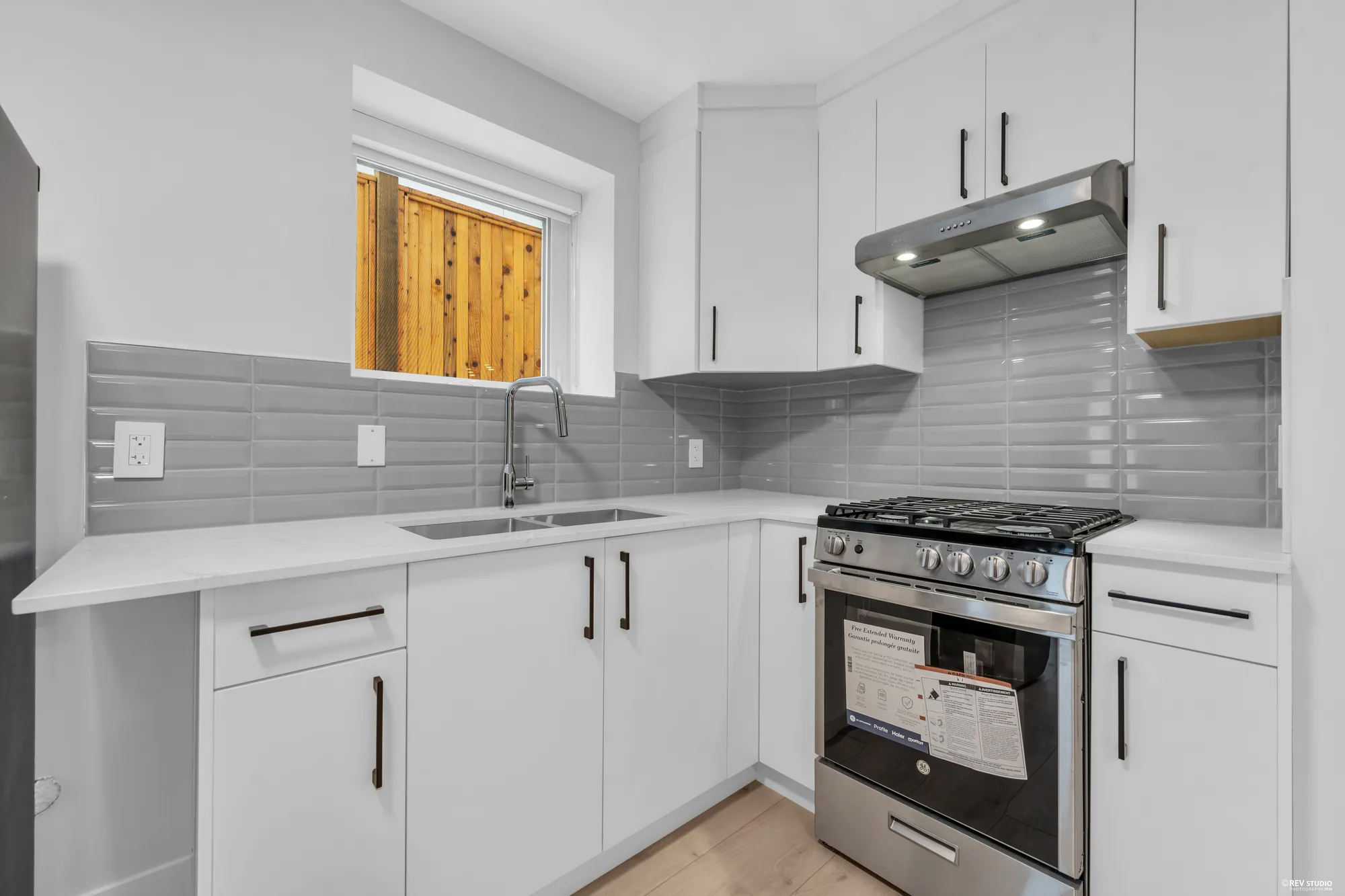 The lower kitchen counter: the sink under the window, a gas range, white cabinets above and below