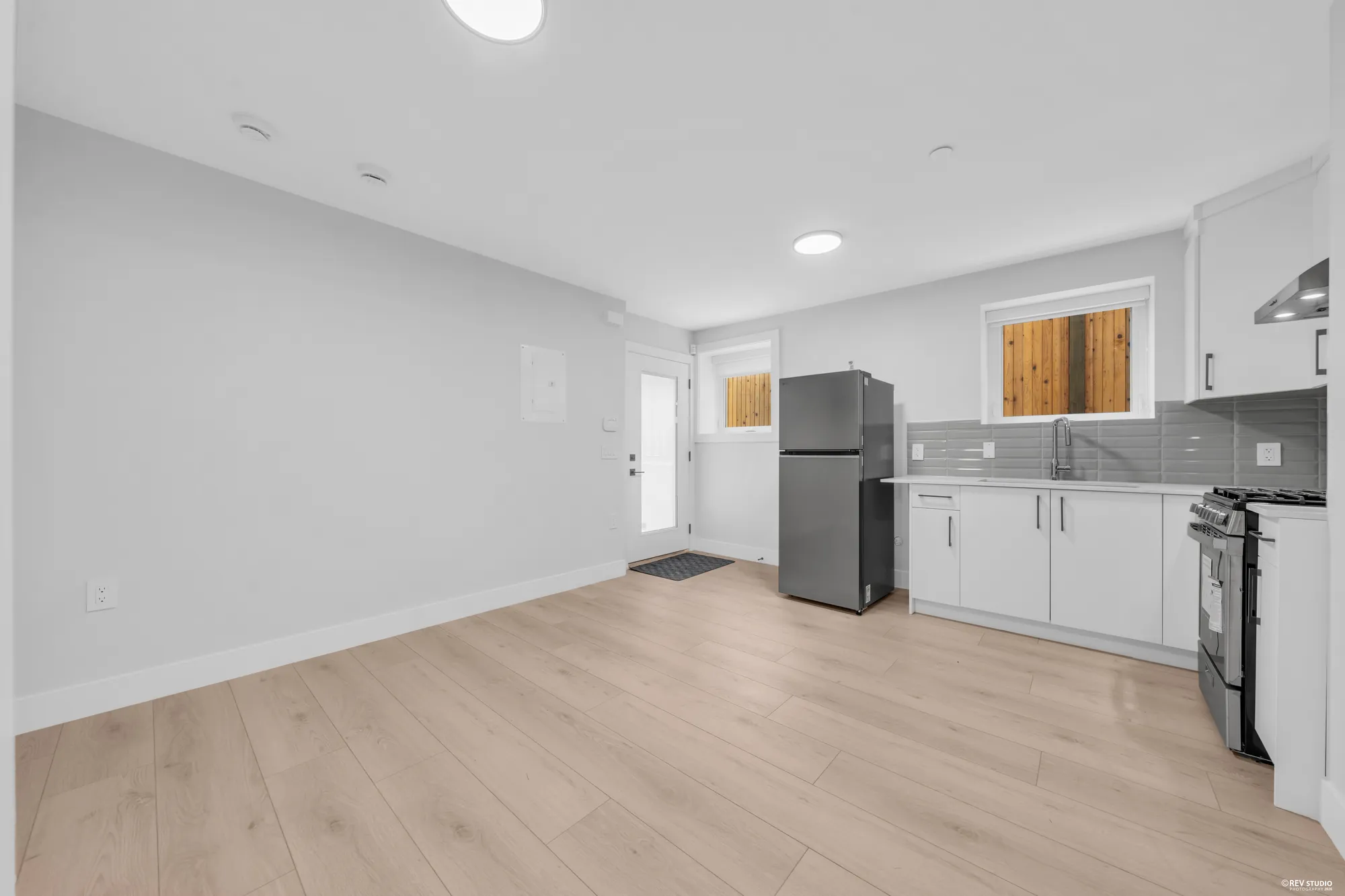 The lower living room: laminate floor, the kitchen counter and fridge along the far wall, the outside door at the end